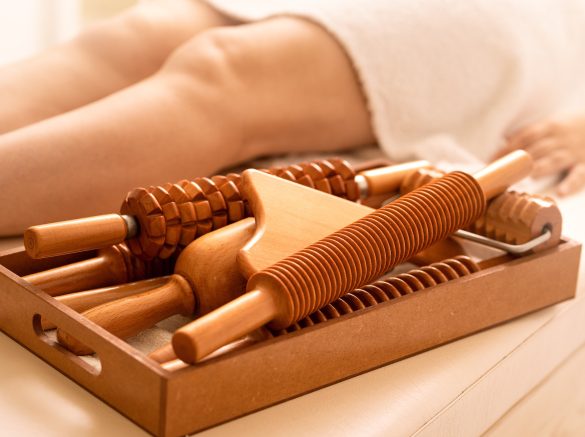 Female on  the massage table next to her is wooden massage tools for Maderotherapy.
